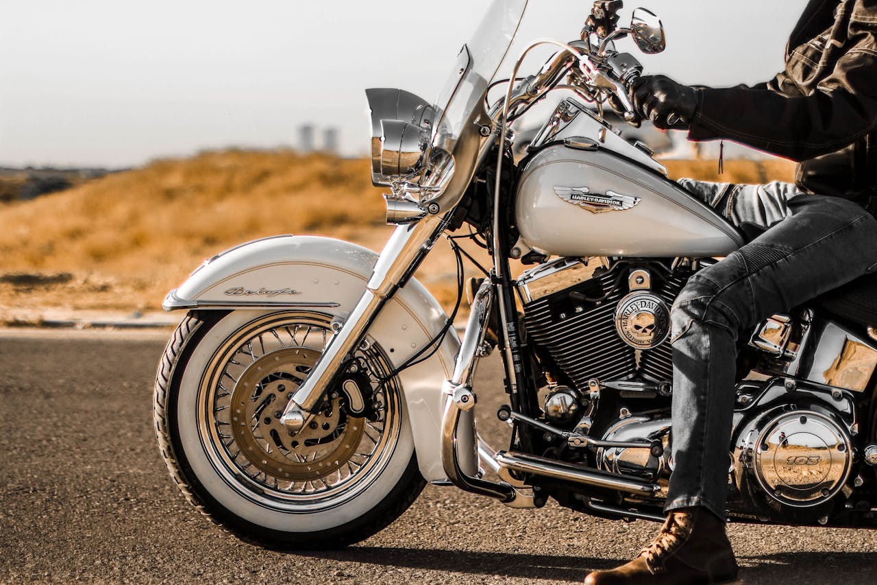 A motorcyclist on a Harley Davidson cruising down an open road under clear skies.